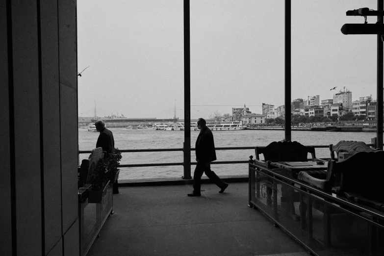 people walking by a window and looking out onto a body of water