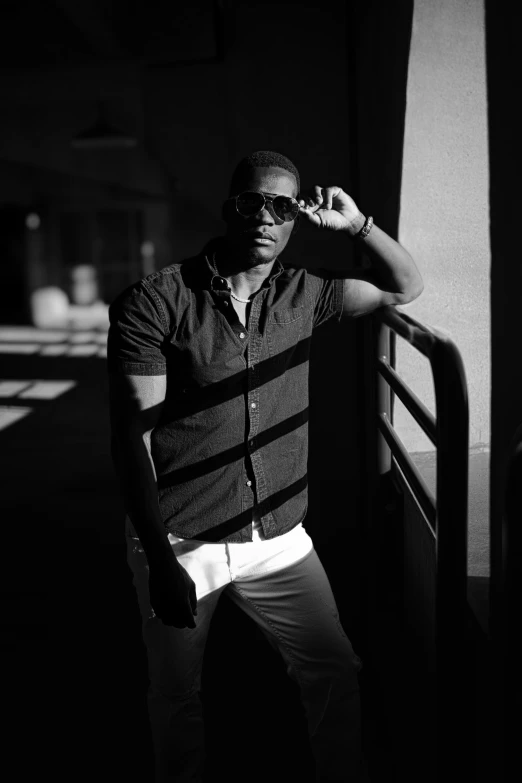 black man wearing shirt standing in front of wall and leaning against rail