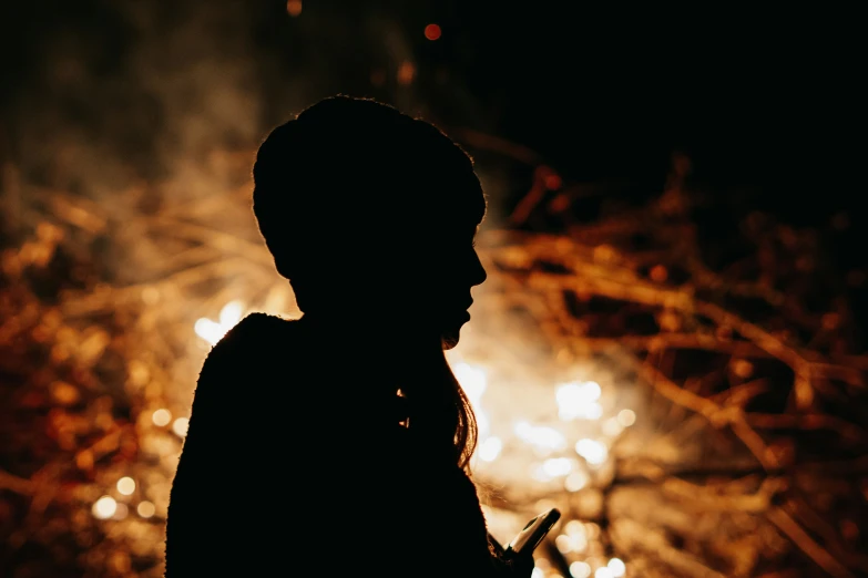 a silhouette of a person holding a cell phone while standing by fire