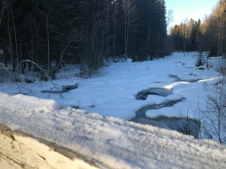 a snowy path with a little river on one side and trees in the other