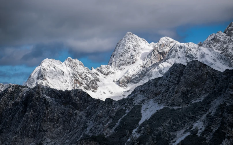 a mountain top with snow capped rocks under a dark cloudy sky