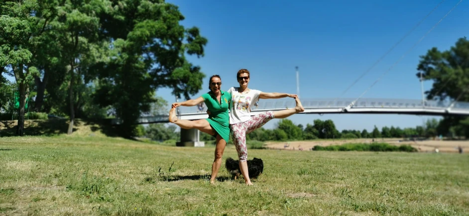 two dancers posing in grass in front of a bridge