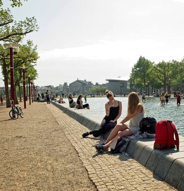 two women sit on a ledge near a body of water