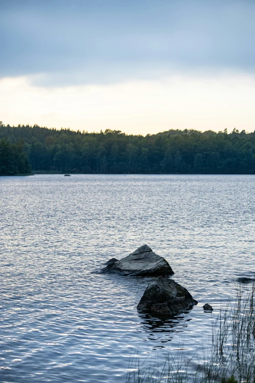 a large rock in a lake with the sky reflected on it