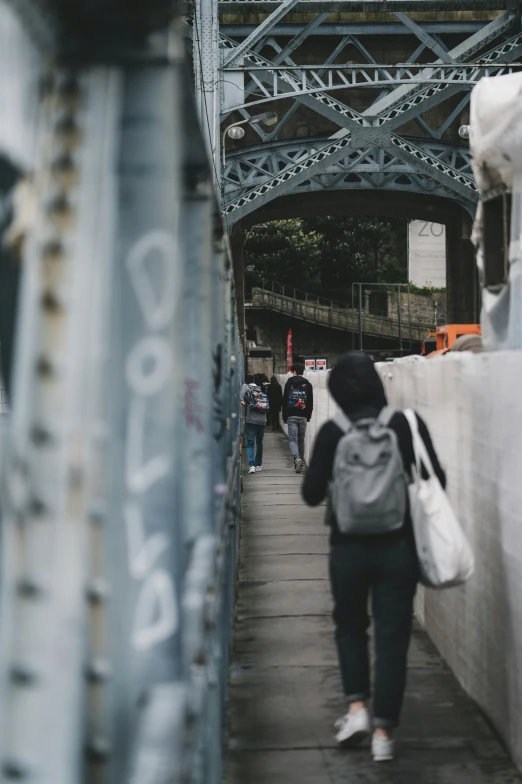 people walking down the sidewalk next to a bridge