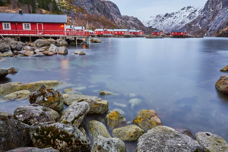 a red building in the background of a lake and some rocks