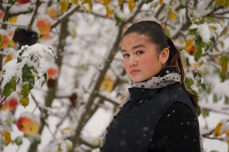 a woman in a black jacket stands by a snowy apple tree