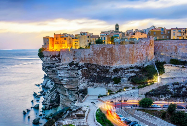 a city on the edge of a cliff with water at dusk