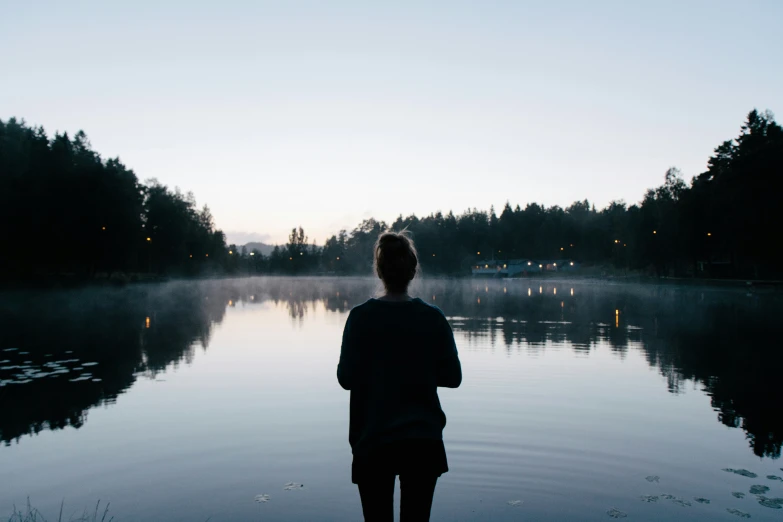 a person standing in front of a lake with trees on both sides