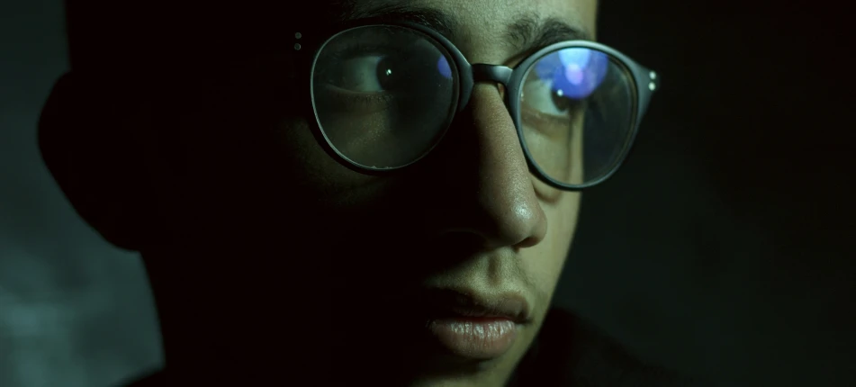 a man wearing circular glasses in the dark
