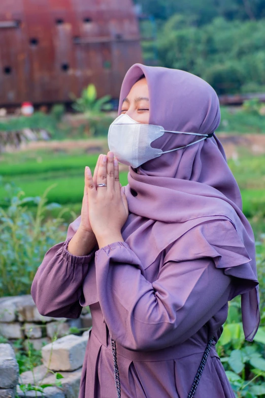 woman in the field prays as she wears a mask