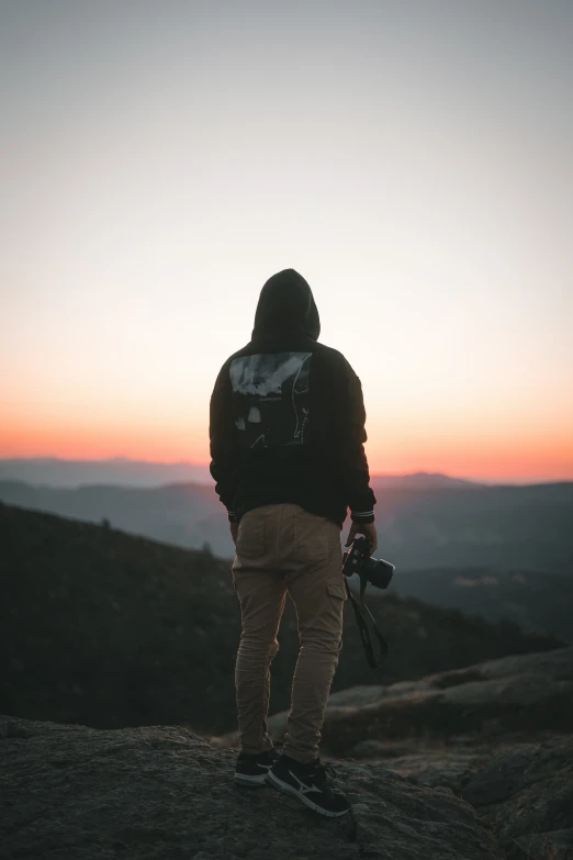 a man stands on the edge of a cliff and looks out at the sunset