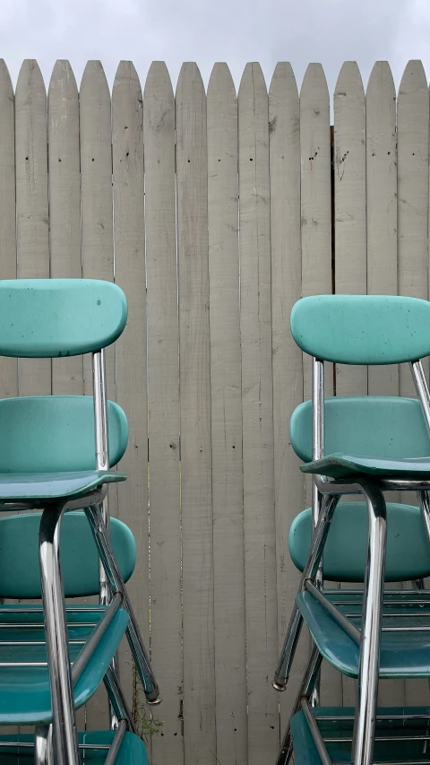 four green folding chairs are lined up against a wooden fence