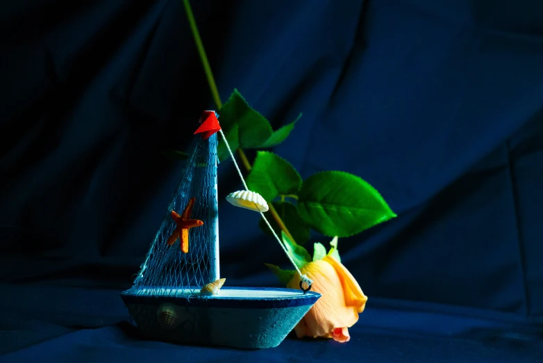 a toy sailboat with a red sail sits next to a plant