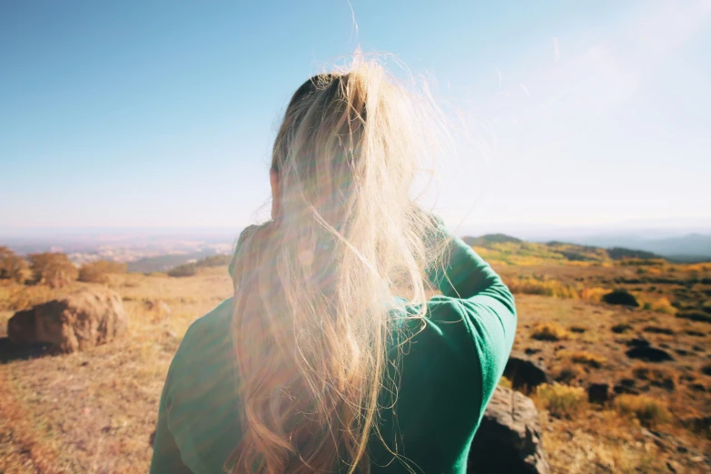 the back end of a person with long blonde hair in a rocky field