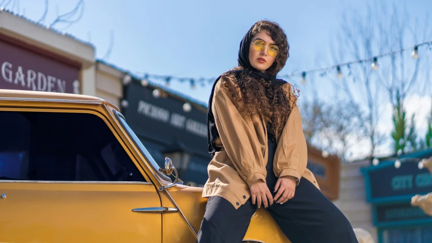 a woman in head covering sitting on top of a yellow car