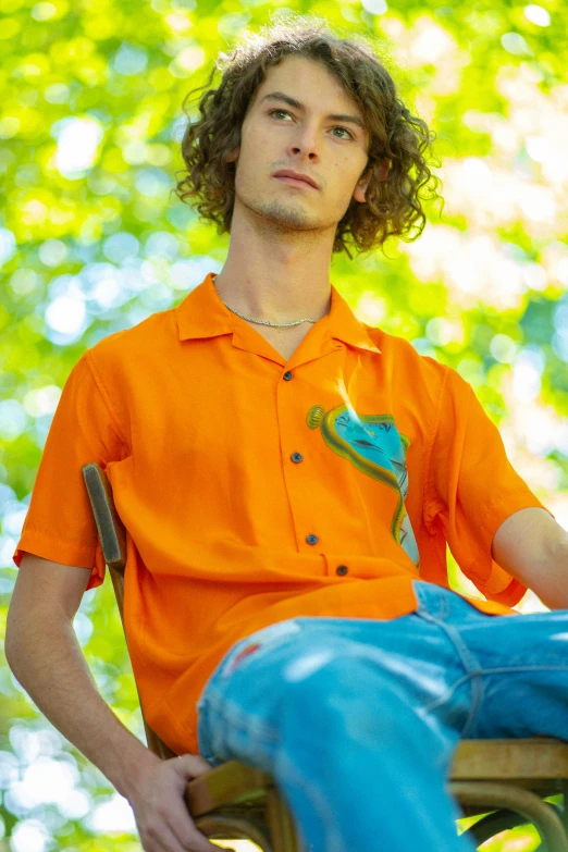 the young man sits in an orange shirt outside