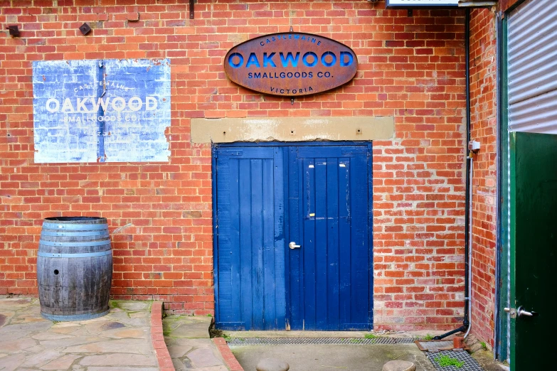 a brick building with a blue door is in front of a barrel