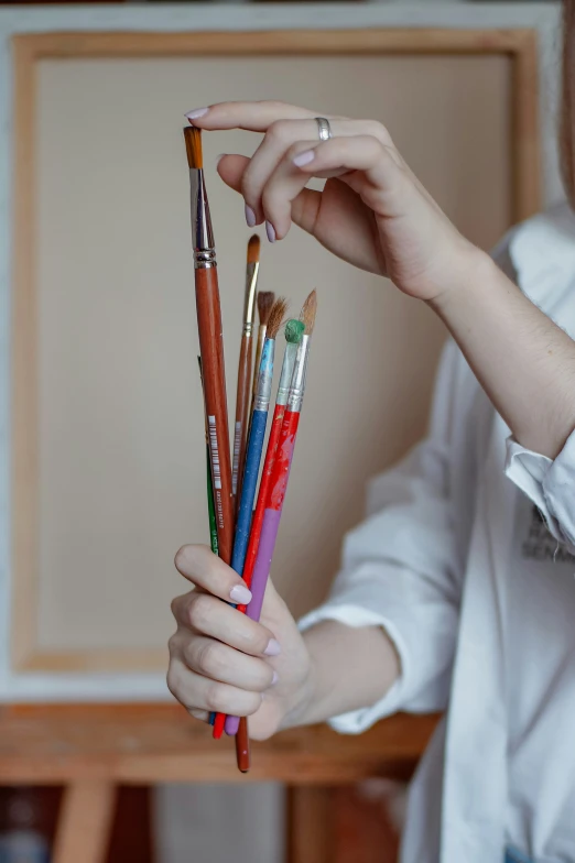 a woman holding several different colored pencils and brushes