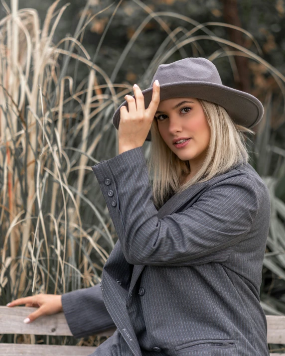 a pretty blonde woman sitting on a bench wearing a hat