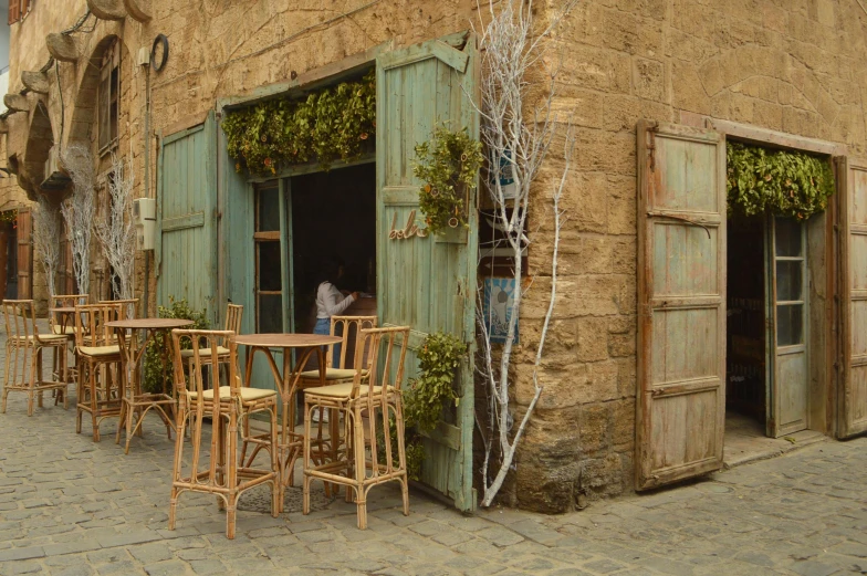 people sit in a small outdoor restaurant with wooden chairs and tables