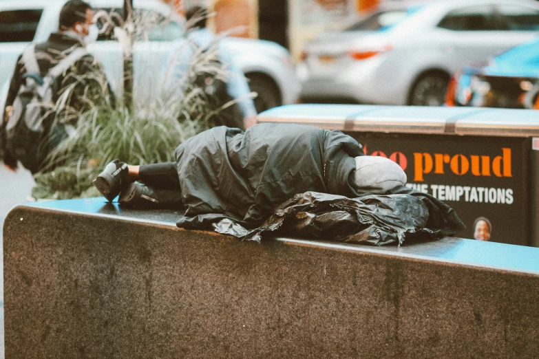 a homeless person lays on the side of a curb