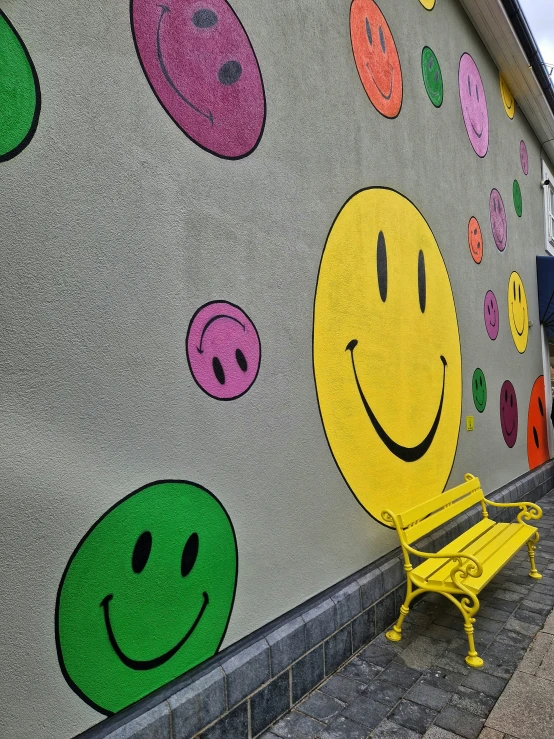 a bench in front of a wall with some colored smiley faces on it