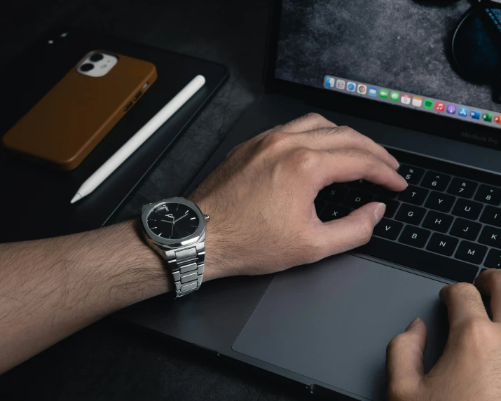 man's hand on laptop computer with wrist watch and phone nearby
