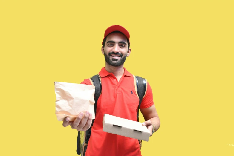 a man with an orange shirt is holding a bag and a pizza box