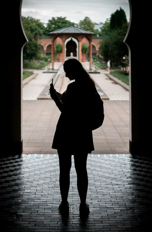 silhouette of woman texting on cell phone in walkway