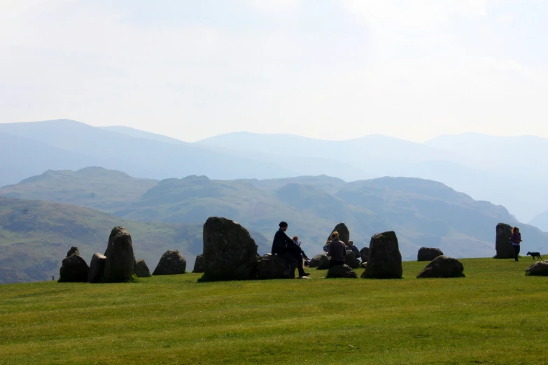 group of people sitting on top of a stonehenge hill