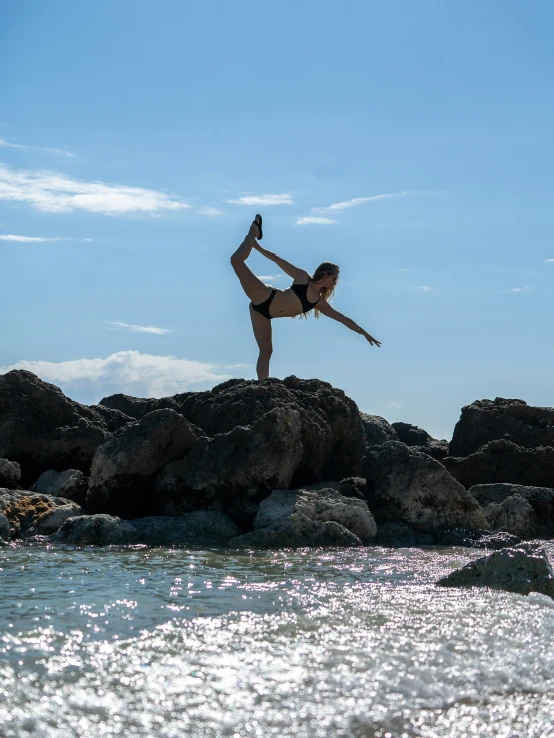 woman doing yoga on rocks next to water