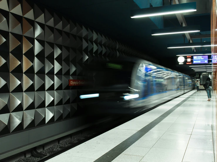 train moving by at underground station with large silver wall