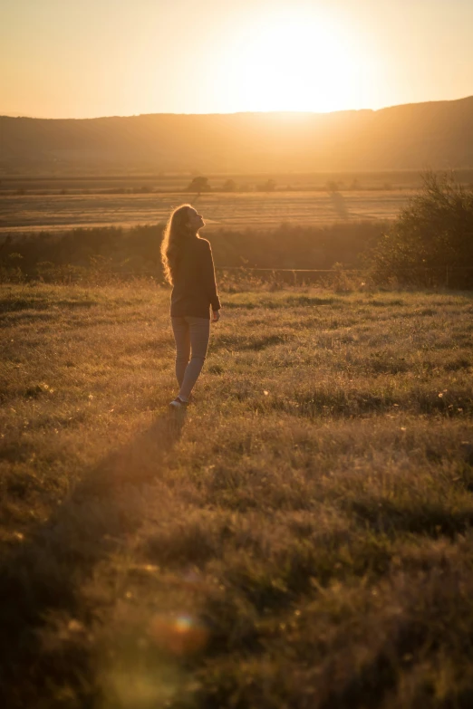 a woman in a grassy field with the sun setting behind her