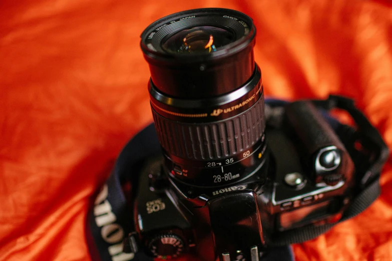 a camera is sitting on a bed that is red and orange