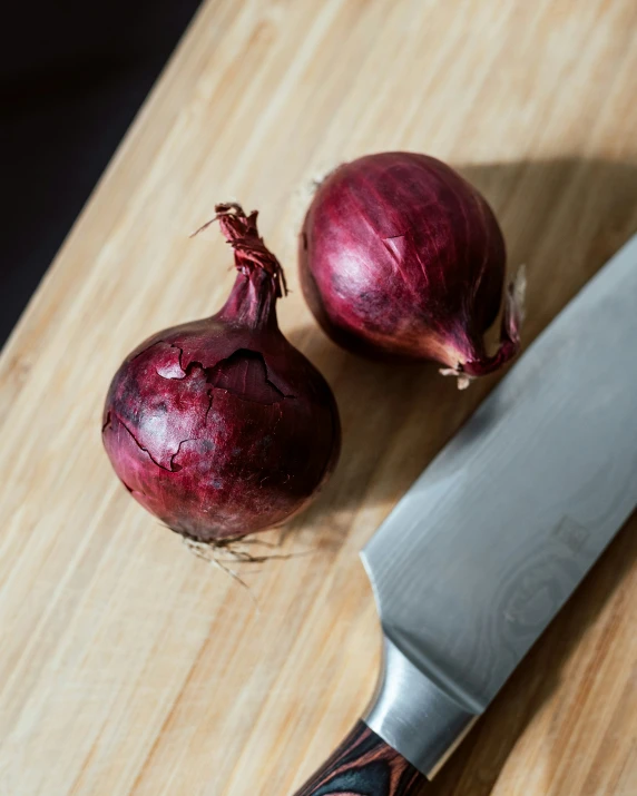 a knife and two pieces of red onion on a  board