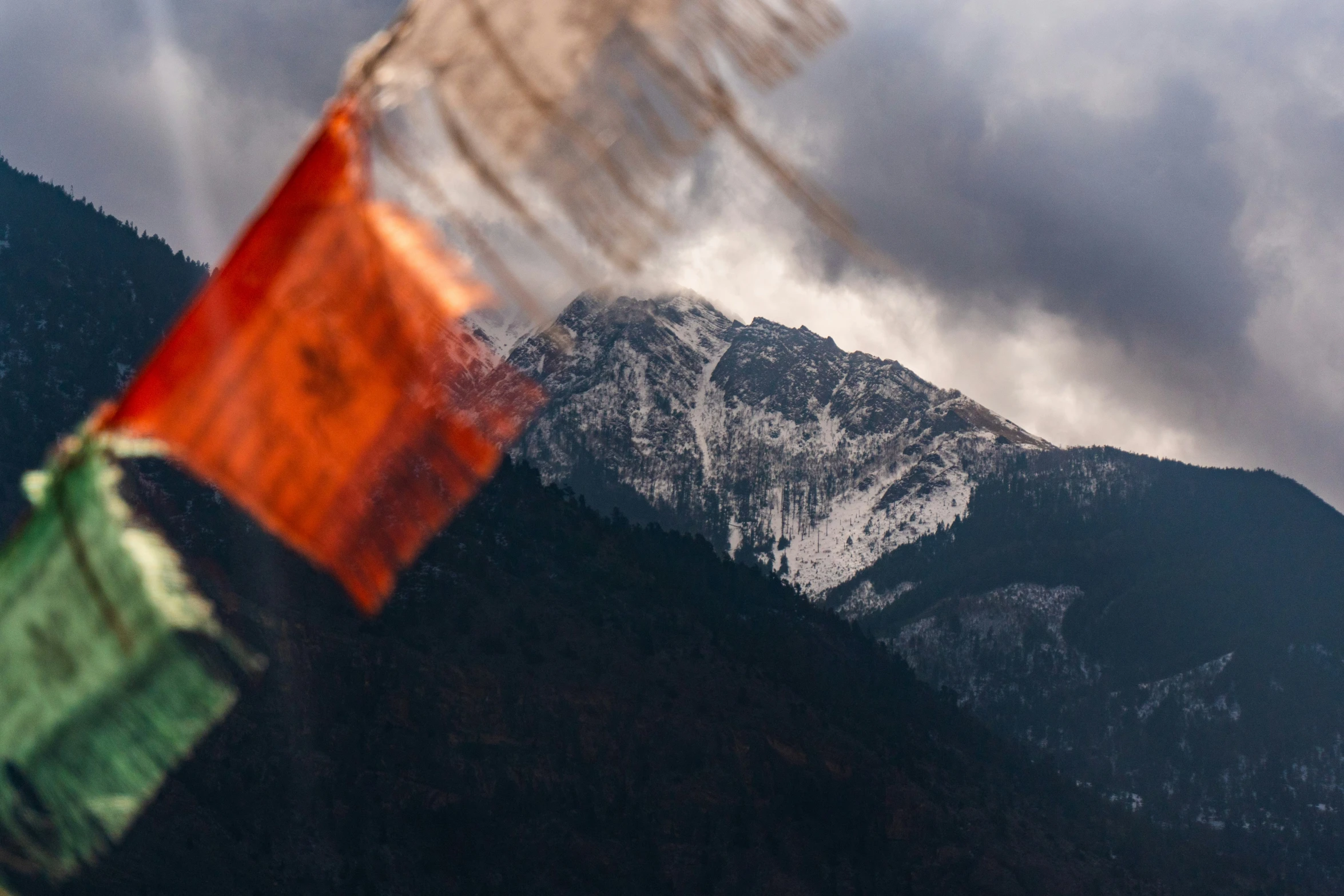 the mountain side shows a red, green and white flag with clouds looming over