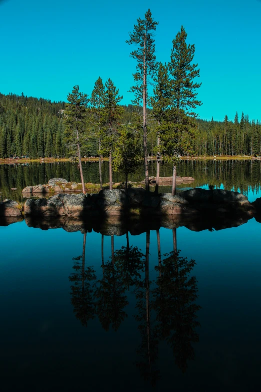 a lake with trees in the background and rocks on shore