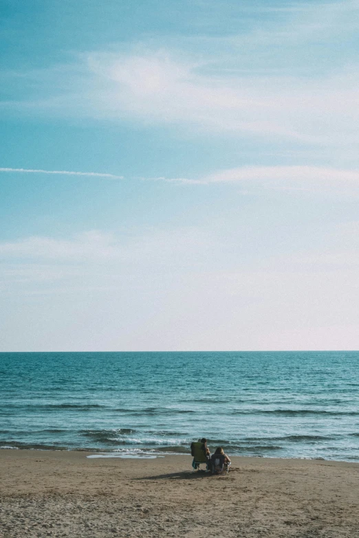 two people sitting on an empty beach under a kite