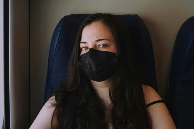 a woman with black face mask sitting in front of a window