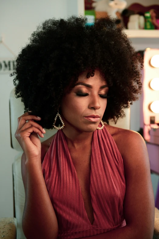 a woman with large afros looking down and holding her hands to her head