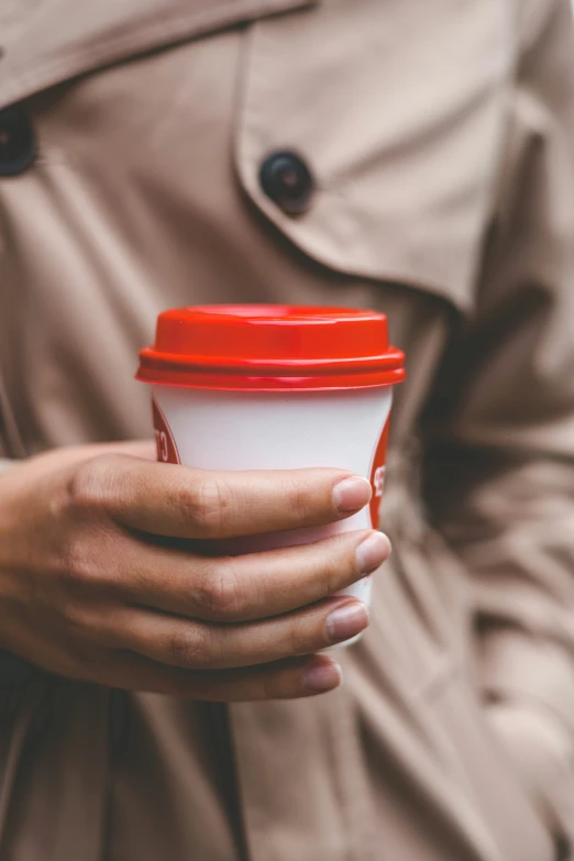 a person holding a coffee cup while standing next to a trench coat