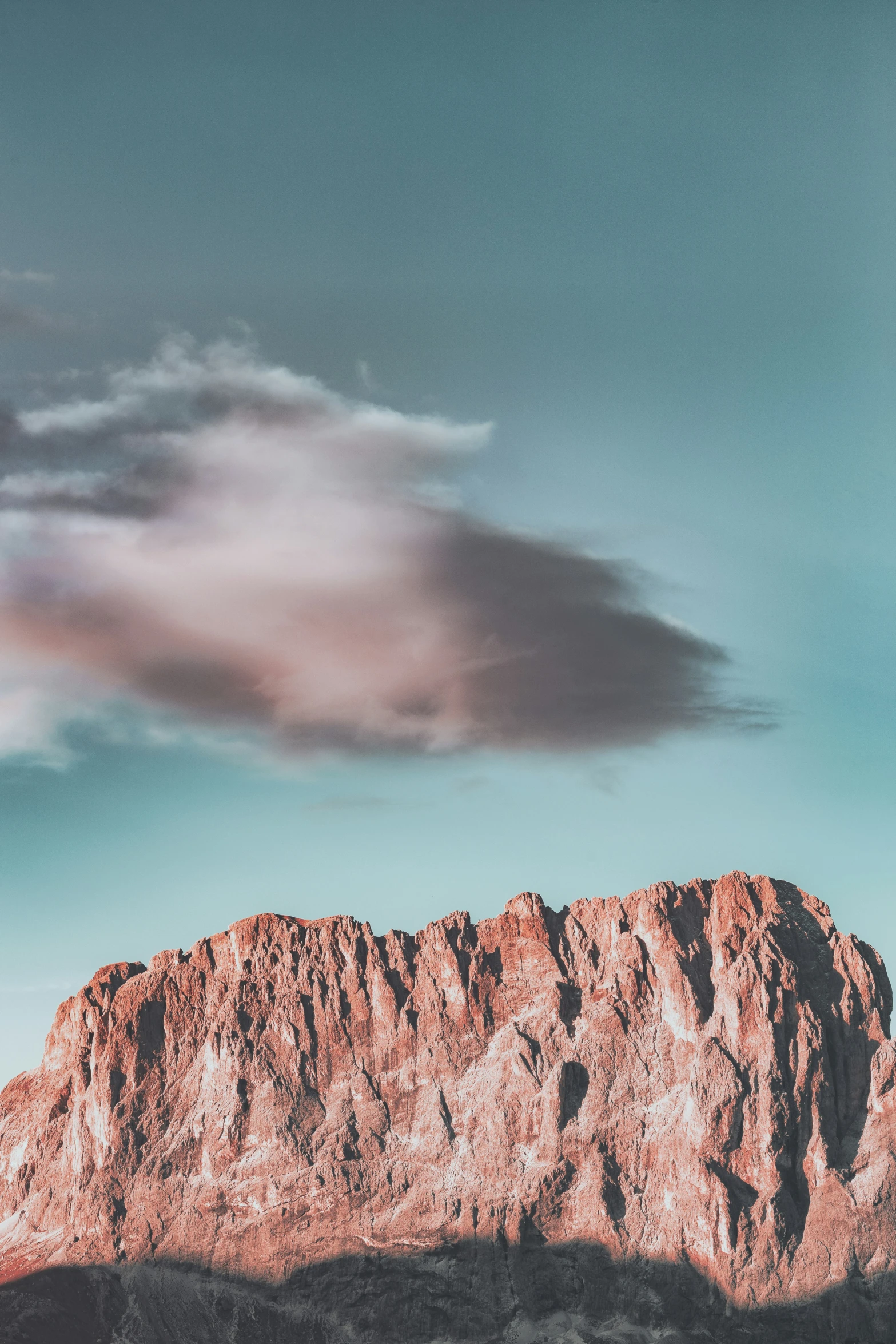 a mountain range with pink clouds and a lone skiboarder