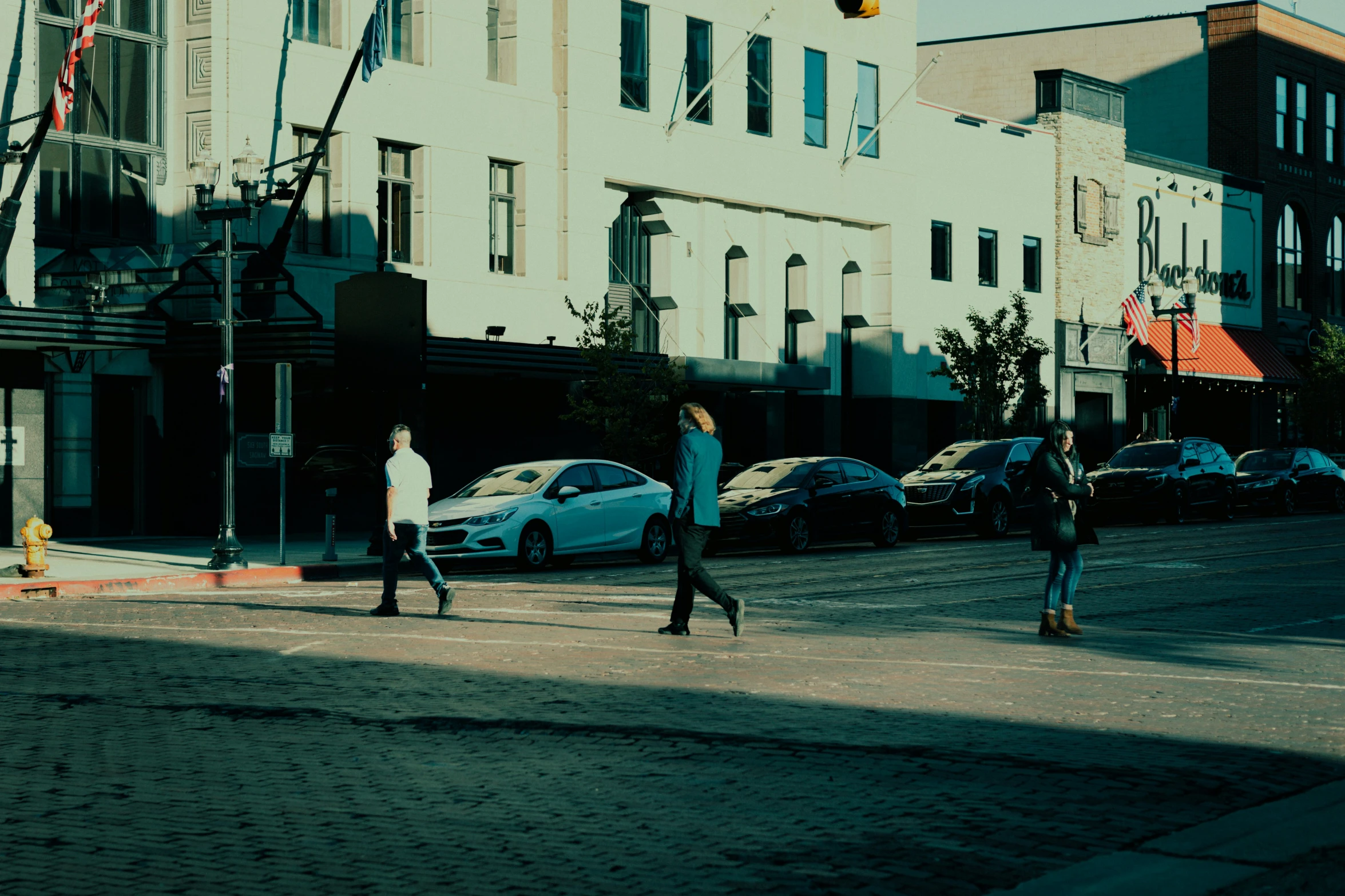 three people crossing the street in front of parked cars