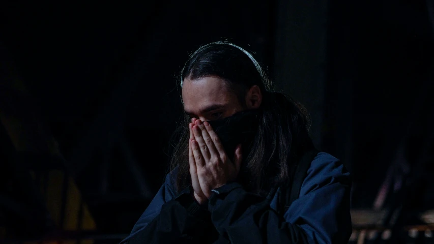 a man with dreadlocks and long hair, covering his eyes, looks off to the side