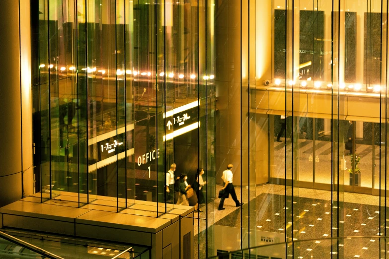 a glass wall at night with people walking in front