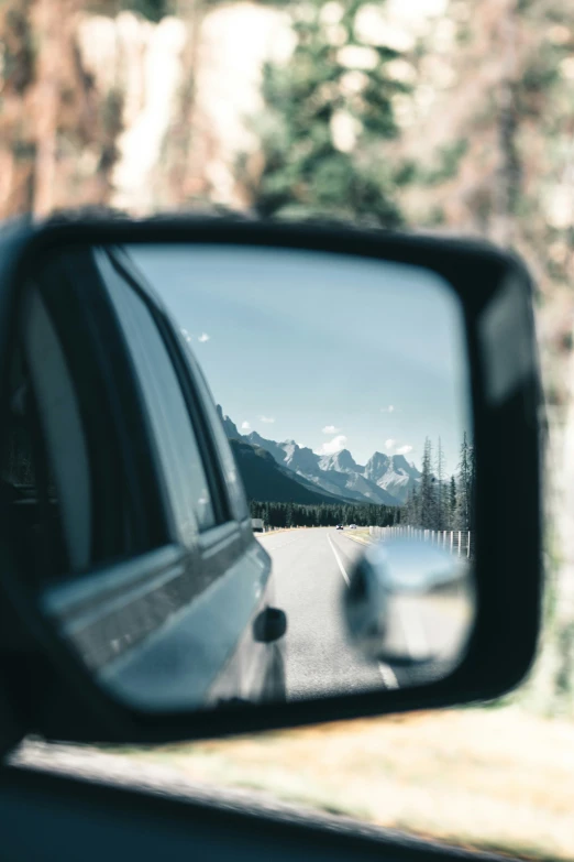 a car's rearview mirror is reflecting the mountains and trees