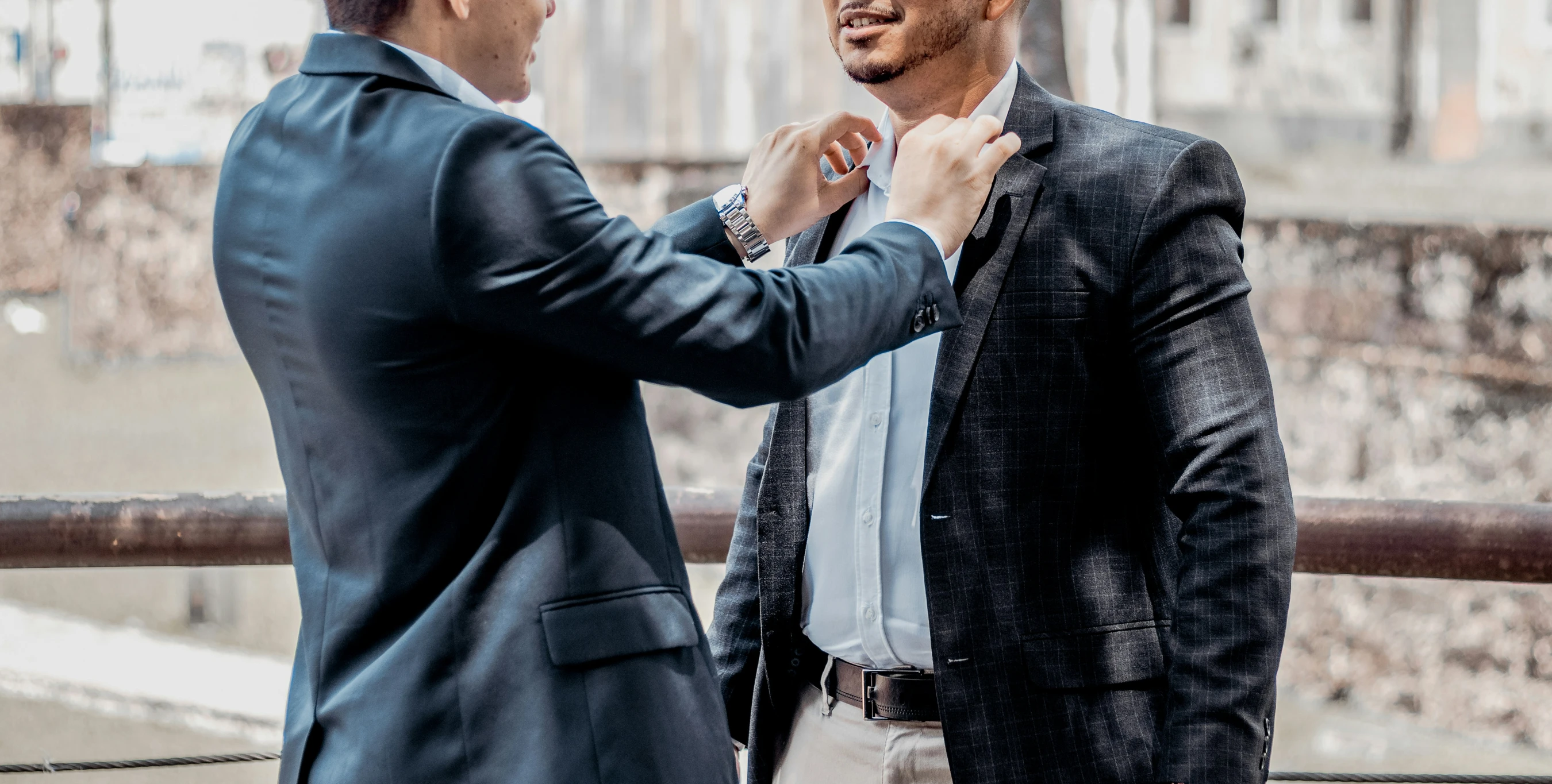 a man adjusting another mans tie next to an old building