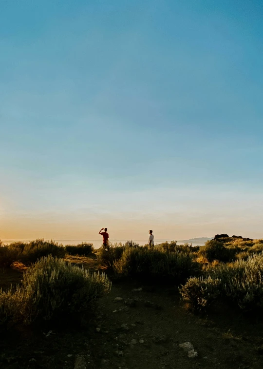 two people stand by the edge of a plain, where there is a small hut, and a body of water near them