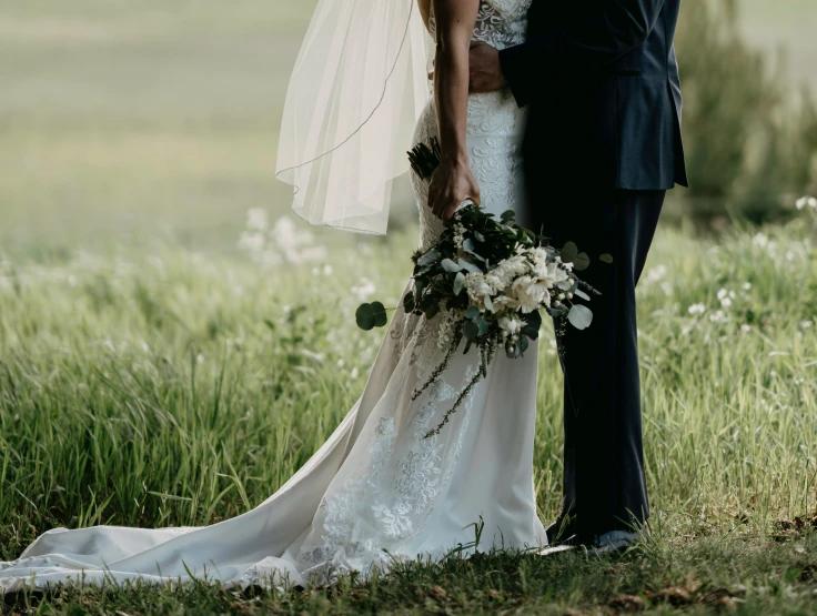 the bride and groom stand in front of a grassy field